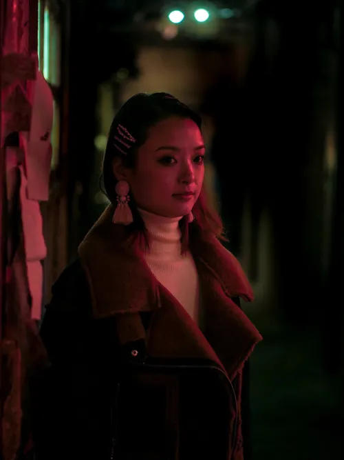 Model lit by red neon in a narrow alley