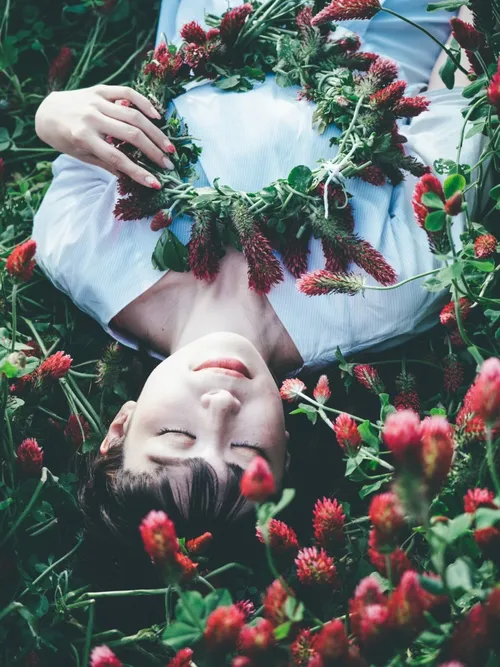 Model lying among red clover in a flower crown
